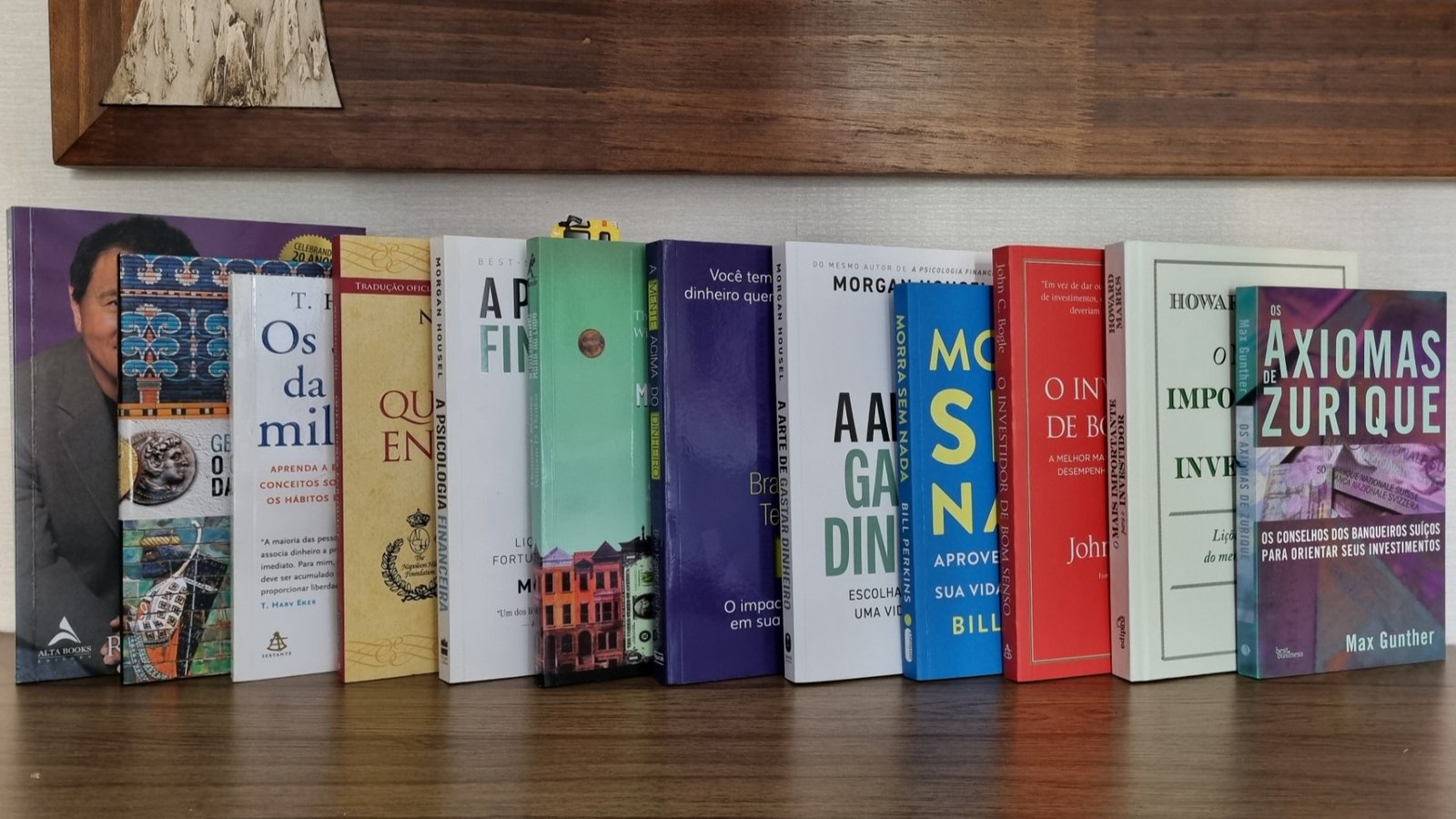 12 livros para investidores iniciantes Foto real de doze livros de finanças e investimentos alinhados lado a lado sobre uma mesa de madeira.