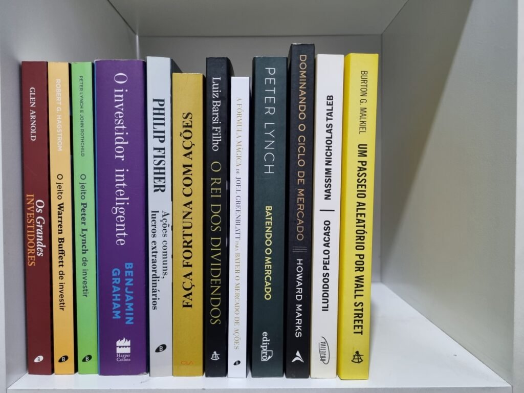 12 livros para criar seu método de investimento Foto real de doze livros de finanças e investimentos alinhados lado a lado sobre uma prateleira.