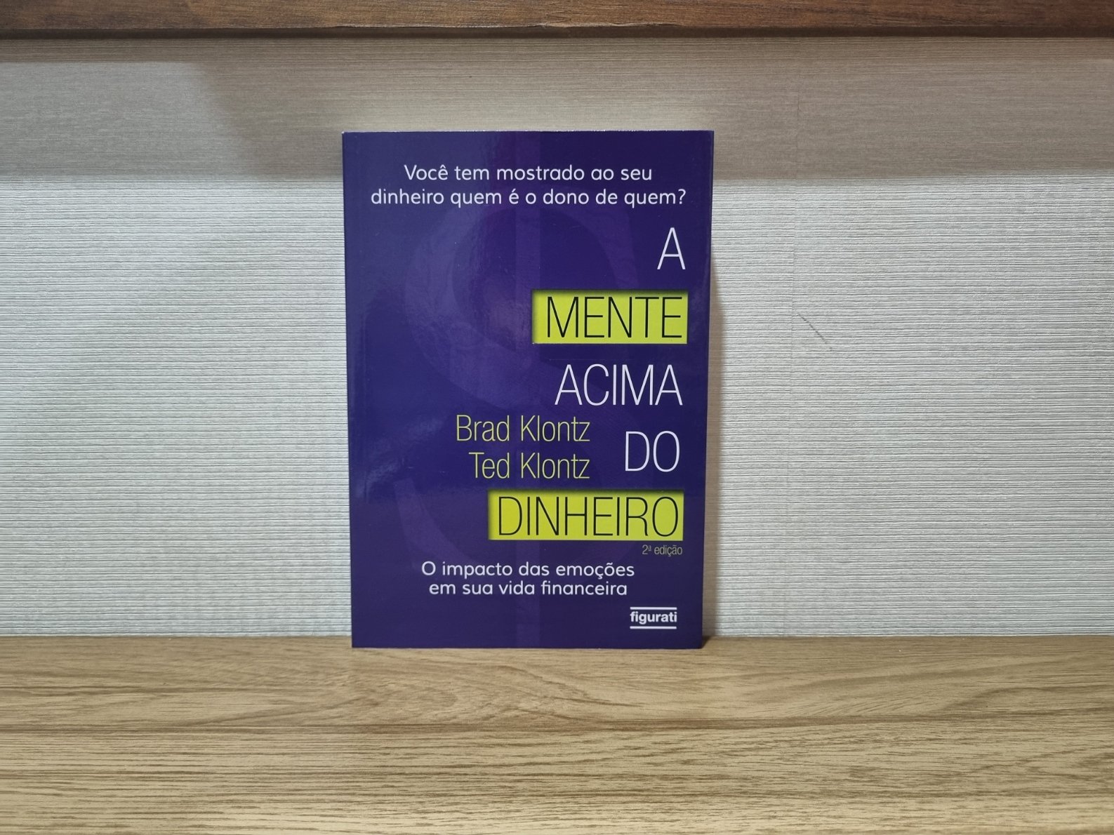 Foto autoral da capa do livro A Mente Acima do Dinheiro de Brad Klontz e Ted Klontz sobre uma bancada de madeira.