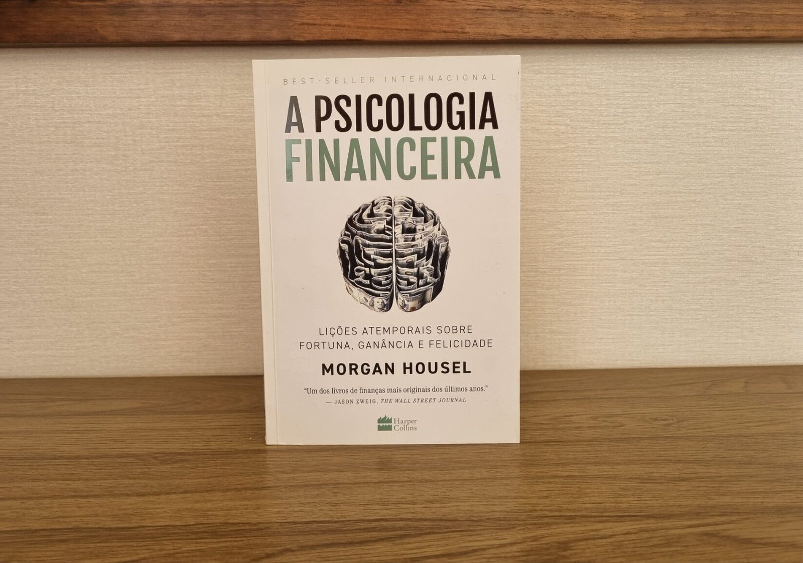 Foto real da capa do livro A Psicologia Financeira, de Morgan Housel, em pé sobre uma mesa de madeira.