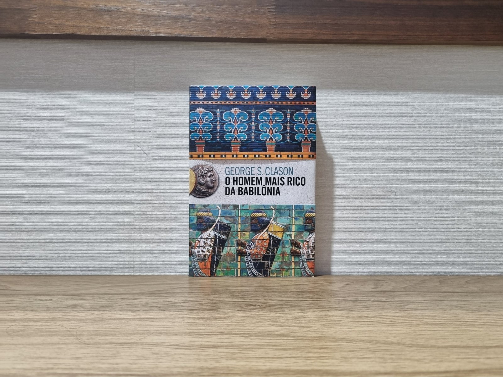 Foto real da capa do livro O Homem Mais Rico da Babilônia de George s. Clason, apoiado sobre uma mesa.
