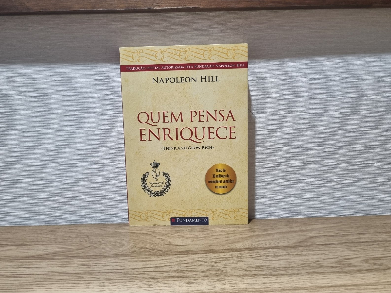 Foto autoral da capa do livro Quem Pensa Enriquece de Napoleon Hill sobre uma bancada de madeira.
