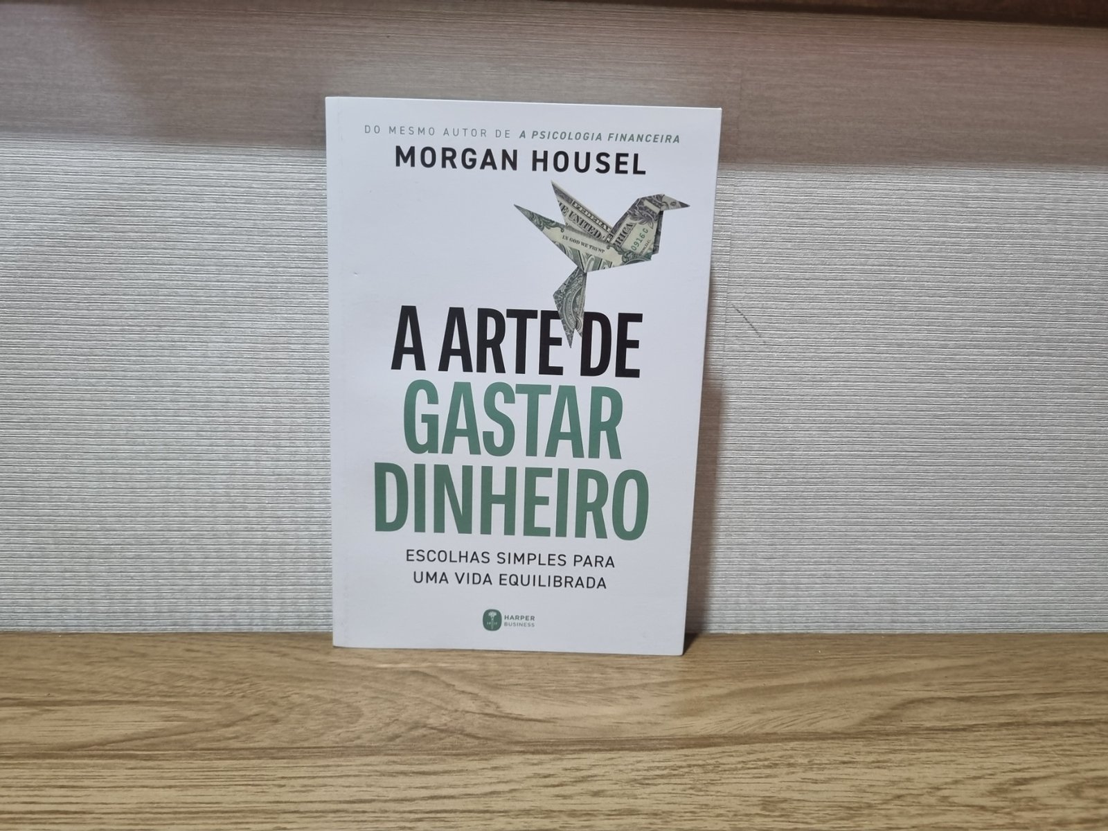 Foto autoral da capa do livro A Arte de Gastar Dinheiro, de Morgan Housel, sobre uma bancada de madeira.
